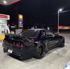 a black car is parked in front of a gas station at night with its hood up