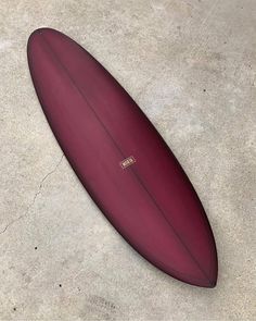 a red surfboard laying on the ground in front of a concrete flooring area