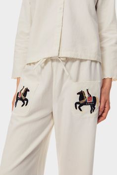 a woman wearing white pajamas with embroidered horses on the side and pockets, both in front of her