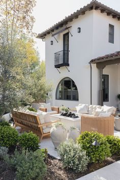 an outdoor living area with couches and tables in front of a white house on a sunny day