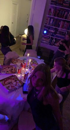 a group of people sitting around a table with pizza on it and candles in front of them