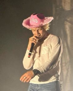 a man wearing a pink hat and holding a microphone to his ear while standing on stage