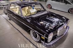 an old black car parked in a garage with its hood up and engine bay open