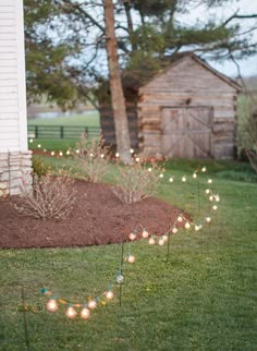 some lights that are in the grass near a building and trees with a house behind them