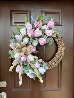 a wreath with pink and white flowers hanging on the front door to a brown door