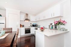 a kitchen with white cabinets and wooden floors is pictured in this image, there are flowers on the counter