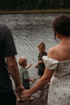 a woman and two boys holding hands by the water