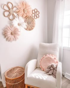 a white chair sitting in front of a window next to a wall hanging with decorative items on it