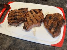 three steaks sitting on top of a cutting board next to a knife and fork