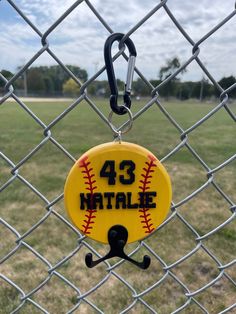 a baseball keychain hanging on a chain link fence with the number 43 natalie written on it