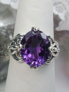 Natural Purple Amethyst RingSmall Fat Oval Design#D111 Inspired by Gothic designs, this stunning antique reproduction ring is crafted in sterling silver. This gorgeous ring is set with a flawless oval-cut natural purple amethyst. The stunning 3 carat weight gemstone is 11mm x 9mm. The band is marked 925 for sterling silver. Notice the beautiful silver filigree swirl setting and band. The bold style travels around the base of the gem and morphs into a solid band. The stunning gem rises above the Elegant Sterling Silver Amethyst Ring Oval Cabochon, Classic Oval Amethyst Ring, Oval Amethyst Ring With Intricate Design, Ornate Oval Amethyst Gemstone Ring, Victorian Style Oval Purple Amethyst Ring, Victorian Style Purple Oval Amethyst Ring, Heirloom Style Oval Amethyst Sterling Silver Ring, Purple Oval Ring With Intricate Design, Oval Purple Ring With Intricate Design