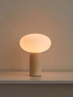 an illuminated table lamp sitting on top of a white shelf next to a beige wall