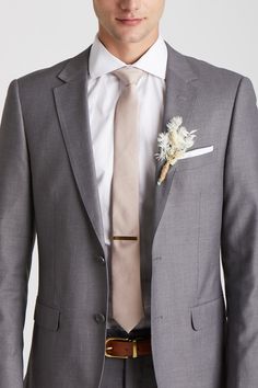 a man in a gray suit with a white flower on his lapel and brown belt