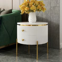 a white and gold side table with flowers on it in front of a green couch