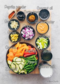 an overhead view of various vegetables in bowls on a cutting board with sauces and condiments