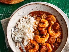 a white bowl filled with shrimp and rice next to a wooden spoon on top of a green table