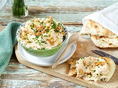 a bowl of chicken salad on a cutting board next to a knife and bread roll