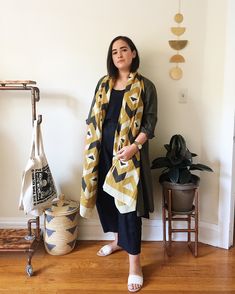 a woman standing in front of a white wall wearing a yellow and black patterned scarf