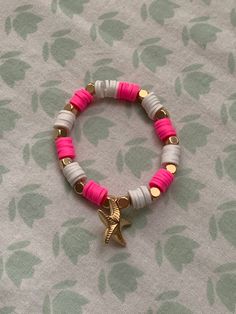 a pink and white bracelet with a gold star charm on it's end, sitting on a floral background