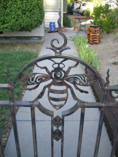 an iron gate with a bee design on the top and bottom, in front of a house