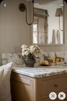 a vase with flowers sitting on top of a marble counter in front of a mirror