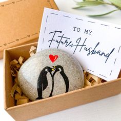 a rock with a penguin painted on it sitting in a box next to a note