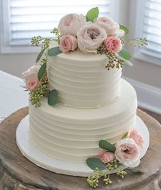 a three layer white cake with pink flowers on top and greenery around the edges