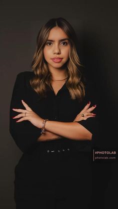 a woman with her arms crossed posing for a photo in front of a black background