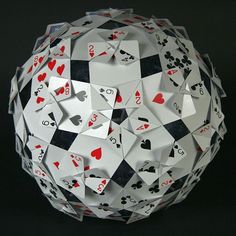 an origami ball with playing cards cut out of it, on a black background