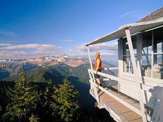 a person standing on the edge of a building looking out at mountains and trees in the distance