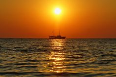 the sun is setting over the ocean with a boat in the distance