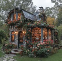 a small house with flowers growing on the windows and doors, surrounded by greenery