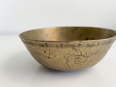 an old metal bowl with writing on the side and numbers etched into it, sitting on a white surface