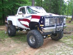 a white truck with an american flag painted on it's hood parked in the woods