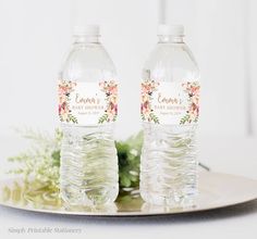 two bottled water bottles sitting on top of a plate next to some flowers and greenery