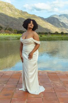 a woman in a white dress standing on a brick walkway next to a body of water