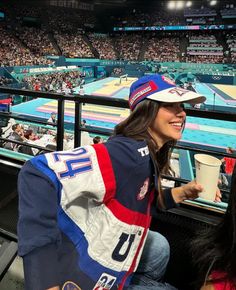 a woman sitting in the bleachers at a baseball game wearing a hat and jacket