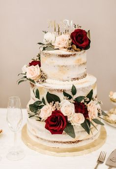 a three tiered cake with red and white flowers on the top is surrounded by silverware