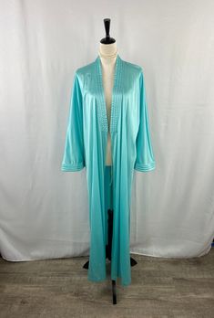 This exquisite vintage Vanity Fair robe is a quintessential piece of retro loungewear that exudes mid-century charm and elegance. Fashioned from a luxurious aqua green satin, this robe showcases the attention to detail and craftsmanship synonymous with the Vanity Fair brand. It features a plush, quilted design along the shawl collar and cuffs, adding texture and a touch of sophistication to the piece. The sash belt cinches at the waist for a flattering silhouette, further accentuated by the flui Retro Fitted Sleepwear For Loungewear, Fitted Retro Sleepwear For Loungewear, Vintage Long Sleeve Loungewear Set, Vintage Long Sleeve Daywear Sets, Vintage Spring Loungewear Robe, Spring Vintage Robe For Loungewear, Spring Vintage Loungewear Robe, Vintage Long Fitted Robe, Vintage Long Sleeve Robe For Loungewear