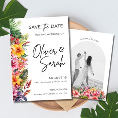 two wedding save the dates cards with tropical flowers and leaves on them next to a wooden plate