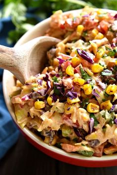 a wooden spoon in a bowl filled with coleslaw and corn salad next to lettuce