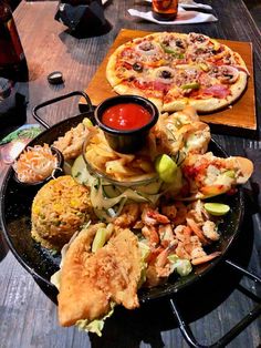 two pizzas and several different types of food on a table