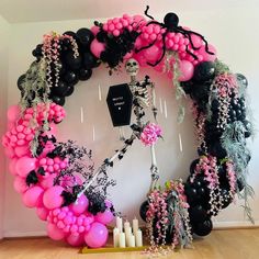 a skeleton is surrounded by pink and black balloons in the shape of a wreath with flowers