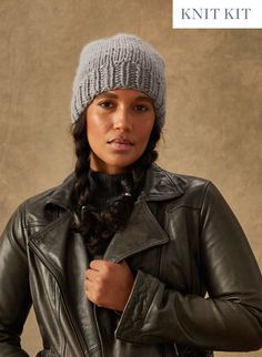 a woman wearing a gray knit hat and black leather jacket with her hands on her hips