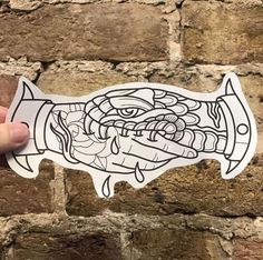 a hand holding up a sticker with an image of a fish in it's mouth