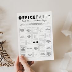 a hand holding up a printable office party game on top of a white table