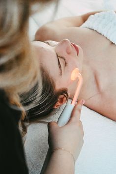 a woman laying on the floor with an electric toothbrush in her hand and another person holding it up to her face