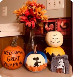 three pumpkins with painted faces on them sitting on a shelf next to a vase filled with flowers