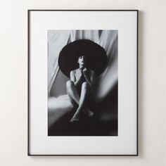 a black and white photo of a woman sitting on a bed with a hat over her head