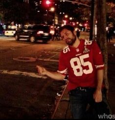 a man in a football jersey is standing on the street corner with his hand out